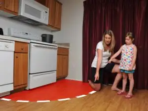 Adult supervising a child following a path marked by paper cutouts on the kitchen floor, creating a playful indoor activity.