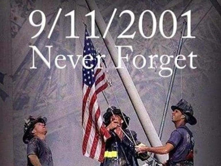 Three firefighters raise an American flag amid debris, with the text “9/11/2001 Never Forget” superimposed over the image, honoring the memory of the September 11 attacks.