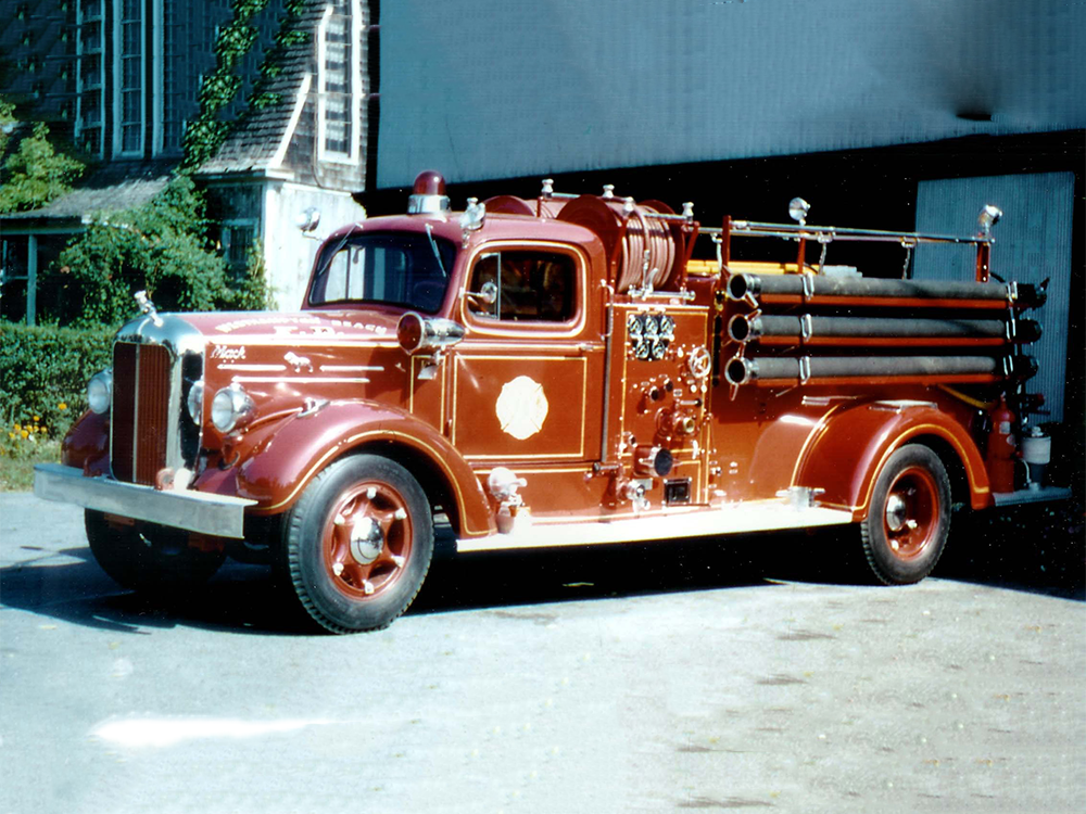 A vintage red fire truck with chrome details and various firefighting equipment is parked outside a building on a sunny day.