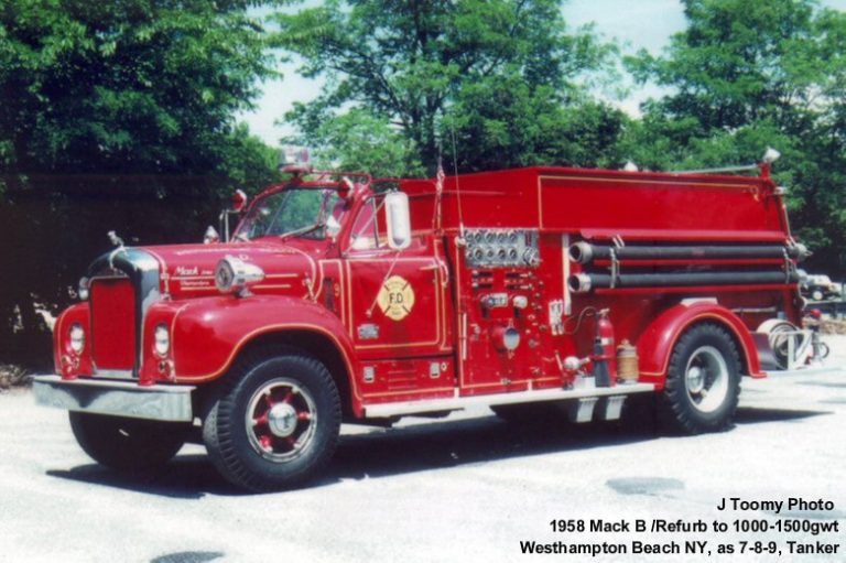 A vintage red fire truck, identified as a 1958 Mack B tanker, is parked outdoors on a sunny day. It features shiny chrome details, hoses, and firefighting equipment. Trees and greenery are visible in the background.