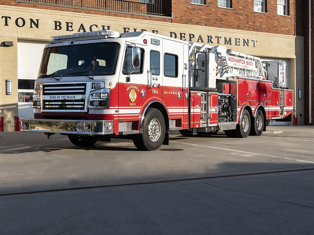 A large red and white fire truck is parked outside a fire station with "FIRE DEPARTMENT" visible on the building. The truck features a ladder and has "SOUTH CITY BEACH" written on the front.